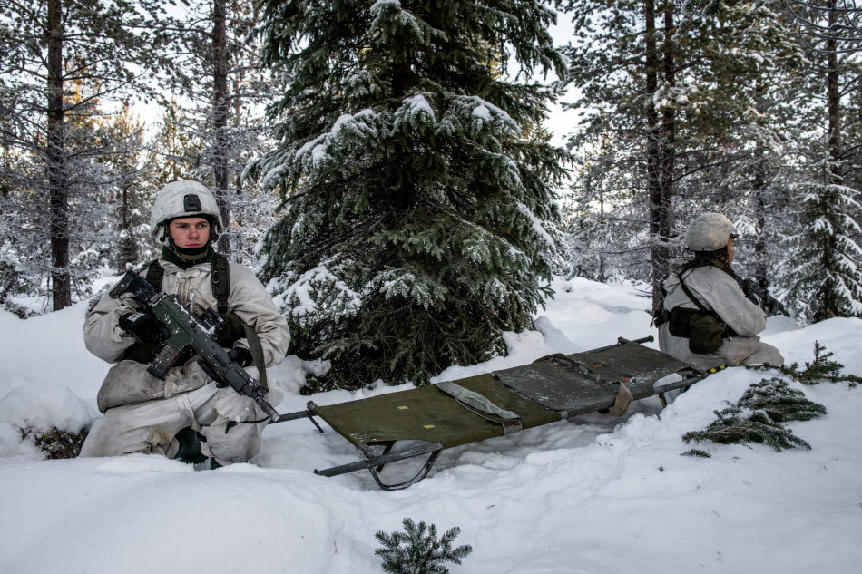 Två soldater i vinterkamouflage vid en transportpulka i en snöig skog.